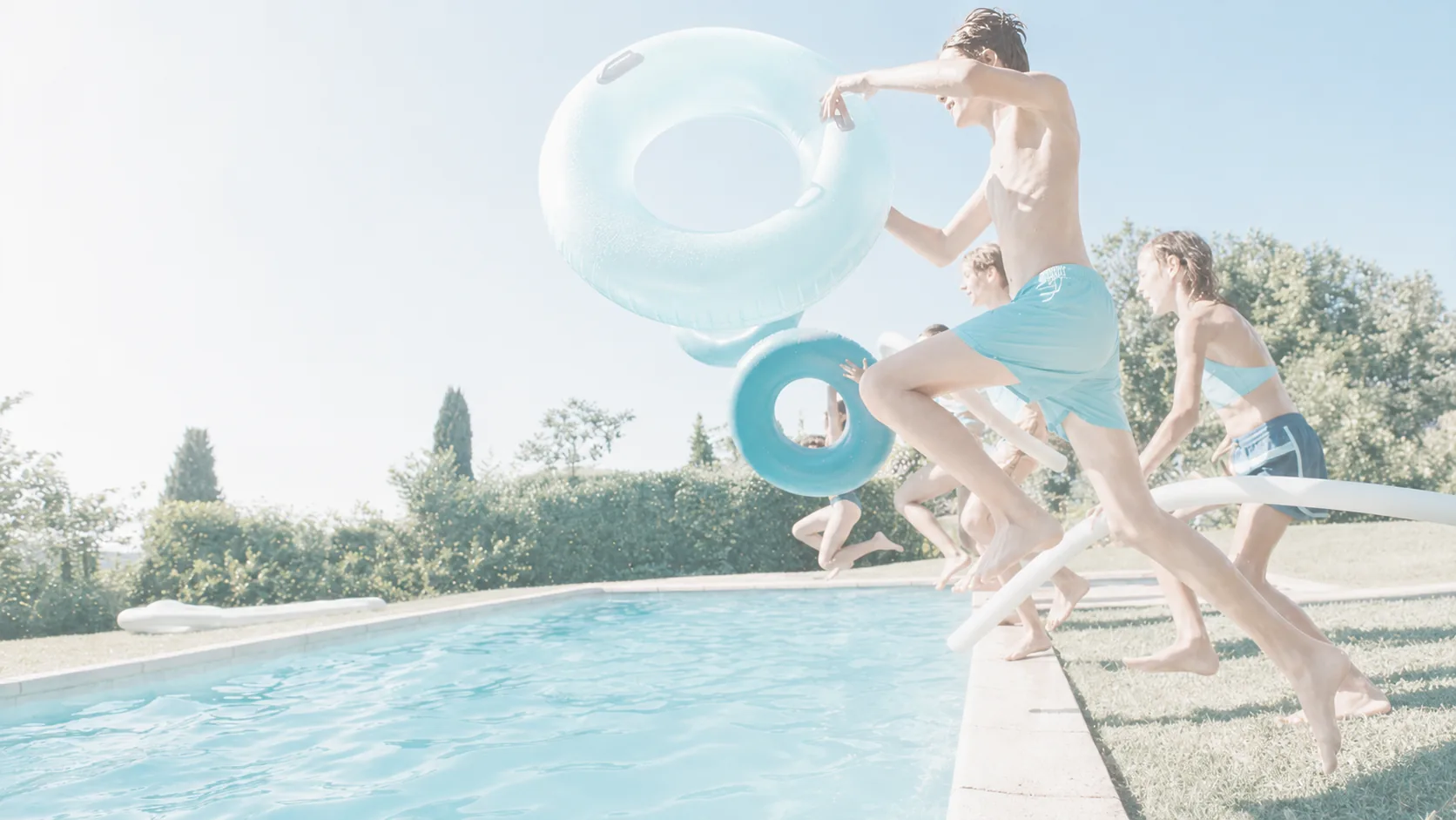 Family enjoying a bright sunny day jumping into a backyard pool